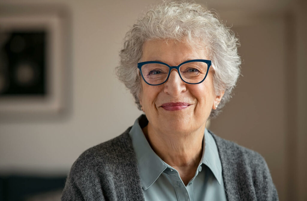 A senior woman with white hair and glasses smiling with wrinkles around her eyes and mouth.