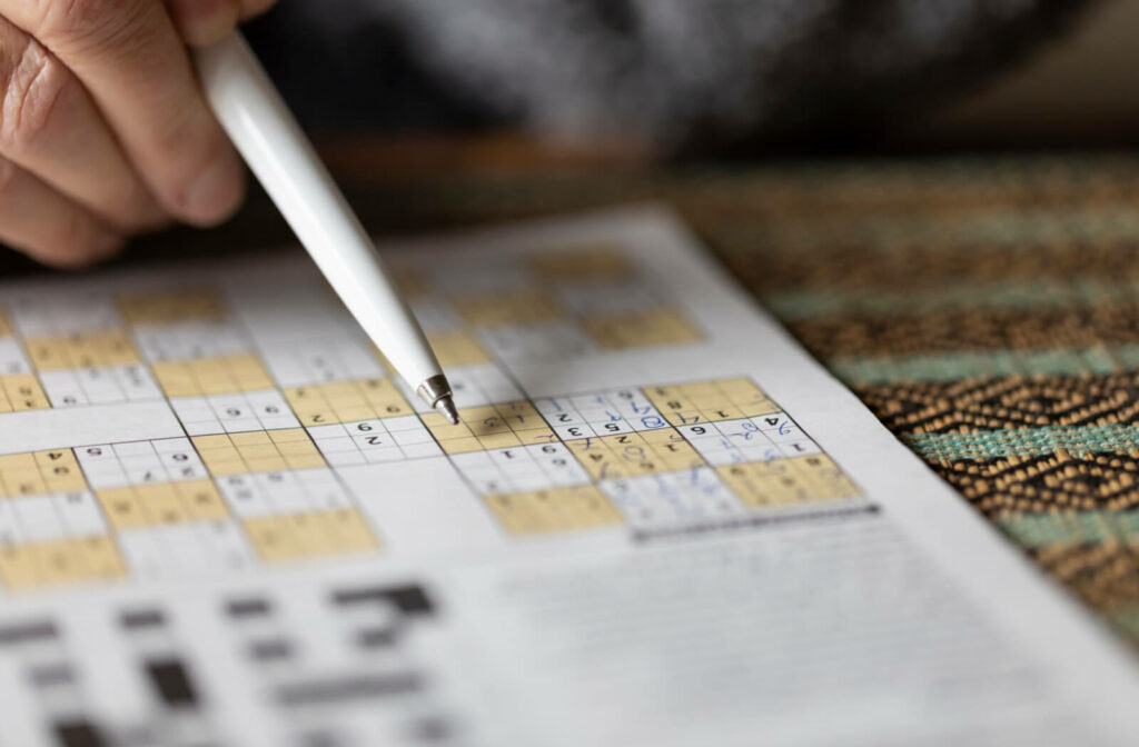 A hand holding a pen pointing at a sudoku brain game on a newspaper.  A great exercise for elderly people to keep a healthy active mind.
