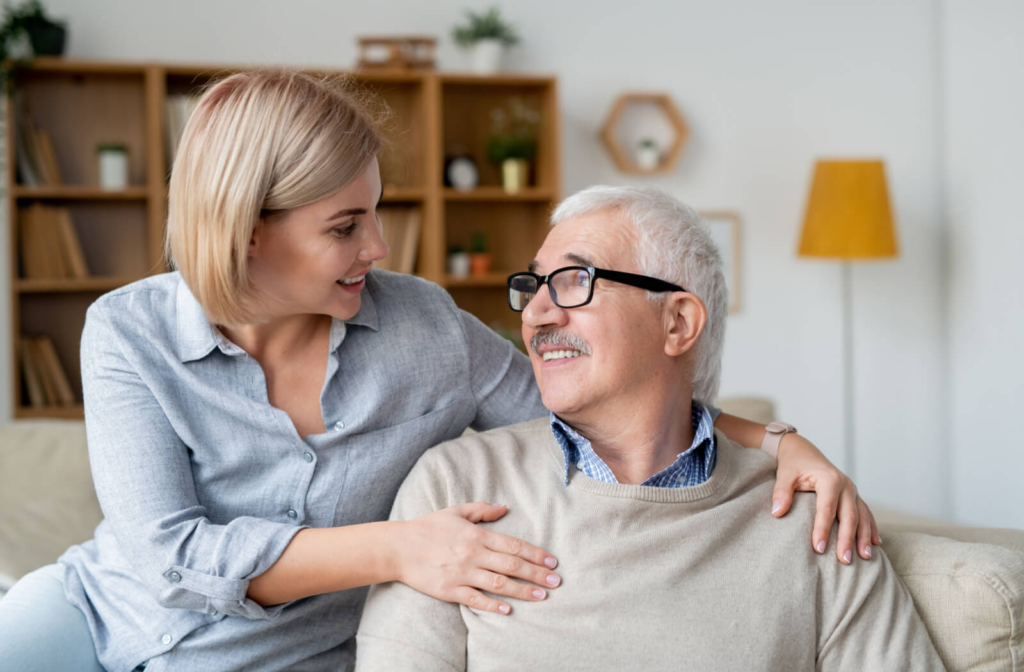 A young woman talking to her senior father about assisted living while they are both sitting on a couch.