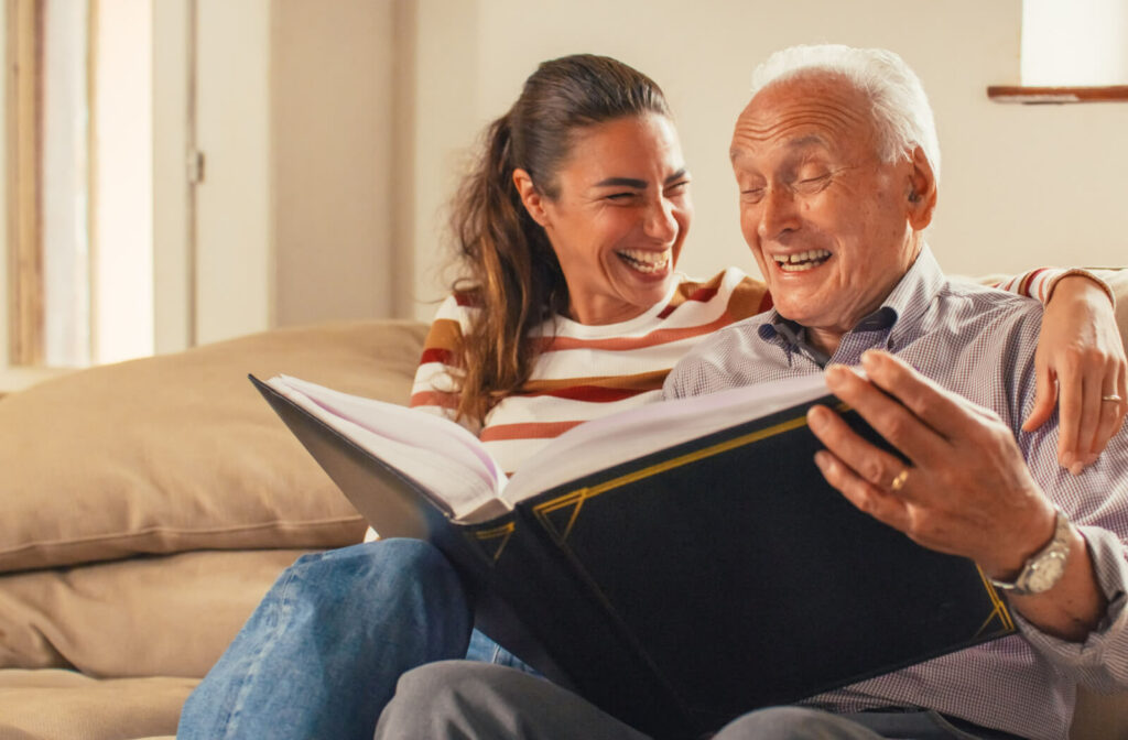 An older adult man and his daughter smiling while looking at a photo album together.