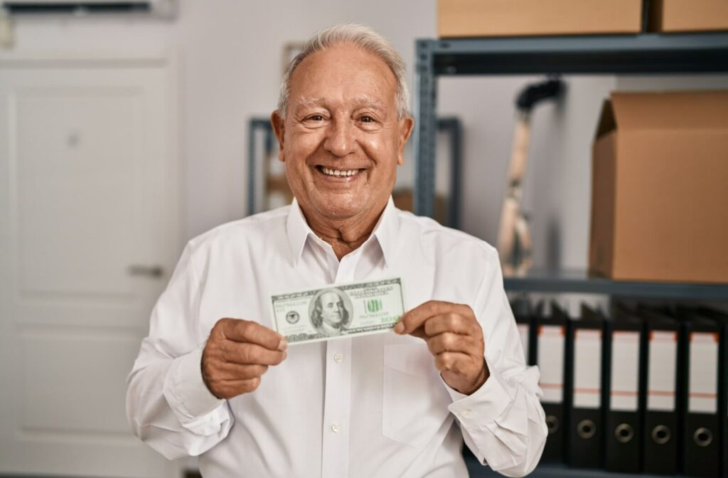 A happy older adult man in a white shirt holding a 100 dollar bill.
