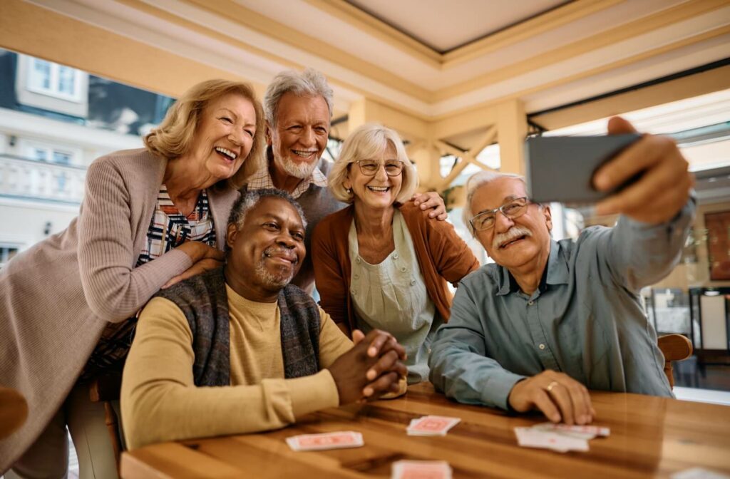 A group of seniors in an assisted living community huddle together around a card table to take a selfie