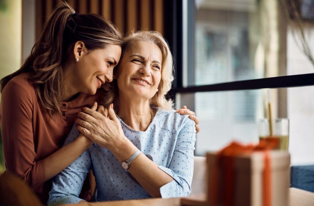 A senior smiles while being being embraced by their adult child.