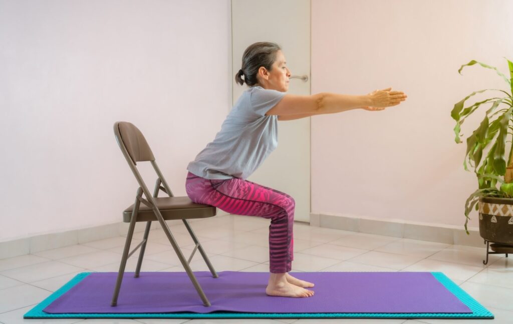 An older adult wearing pink leggings uses a chair to do some chair-assisted squats to improve their leg strength.