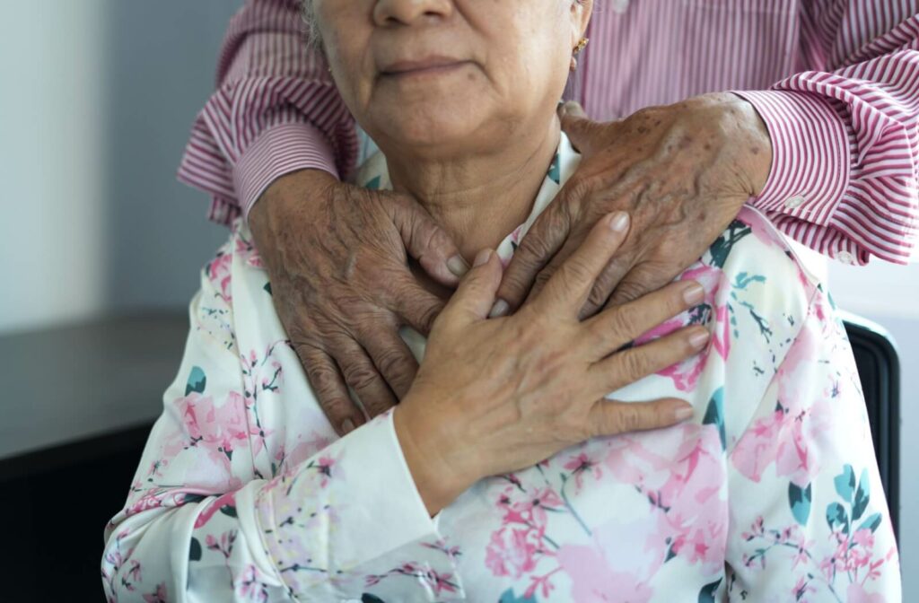 Elderly person in floral robe with older hands gently resting on her shoulders