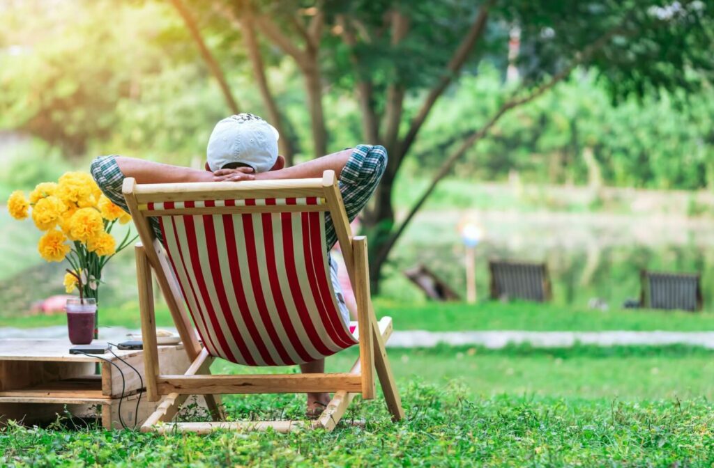 Senior enjoying summer safely outdoors relaxing in a shaded area in a striped chair with flowers and greenery nearby