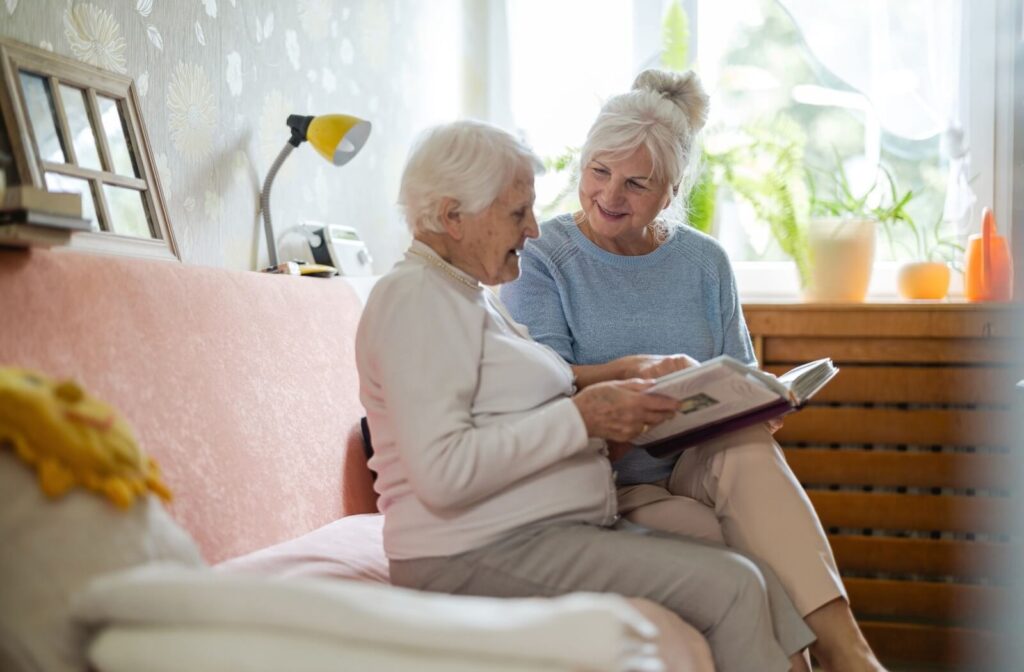 An older adult and their friend sit together on a couch in memory care and flip through a photo album together